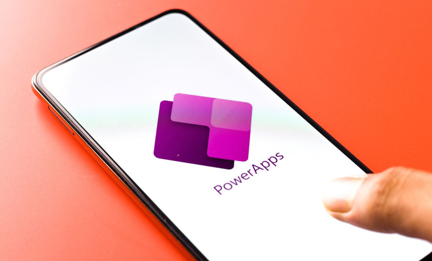 Smartphone so zobrazeným logom Microsoft Power Apps v ruke používateľa – symbol moderného low-code vývoja, mobility a jednoduchej tvorby firemných aplikácií na mieru.