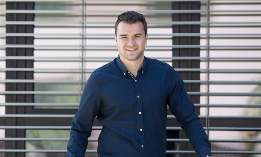 Portrét usmívajícího se mladého profesionála v tmavé košili před moderní fasádou s žaluziemi – symbol ambicí, růstu talentů a moderního pracovního prostředí ve skupině Seyfor.