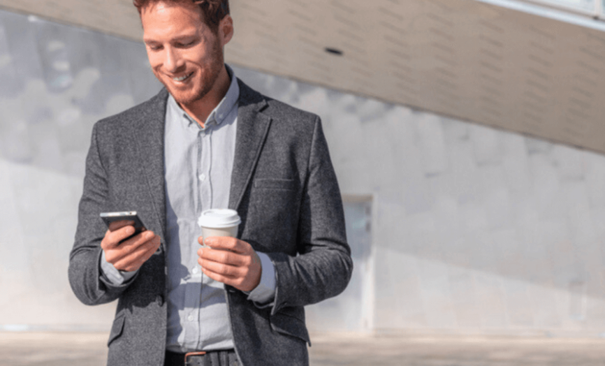 Muž v šedém saku, s kávou a telefonem v rukách