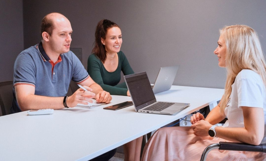 Dvě ženy a muž sedící u pracovního stolu v kanceláři