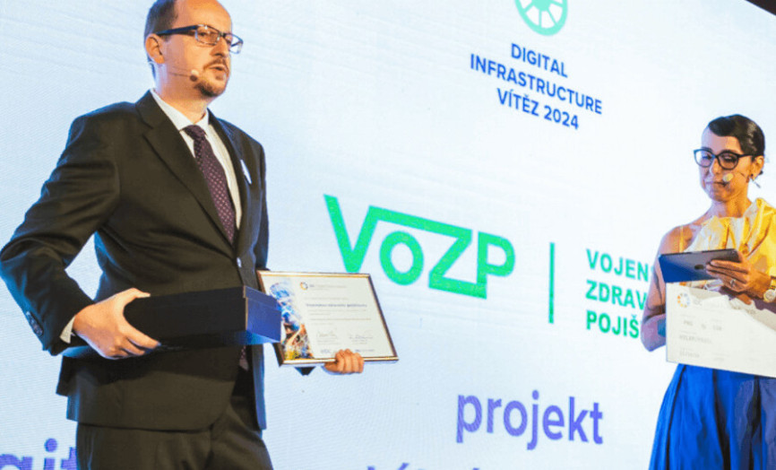 Zástupce VoZP přebírá ocenění Digital Infrastructure Vítěz 2024 před prezentační stěnou.