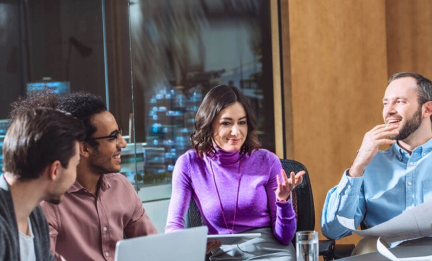 čtyři lidé debatující u pracovního stolu s notebooky