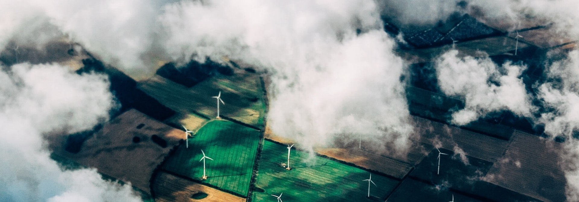 Letecký pohled na větrné elektrárny mezi poli částečně zakrytými mraky