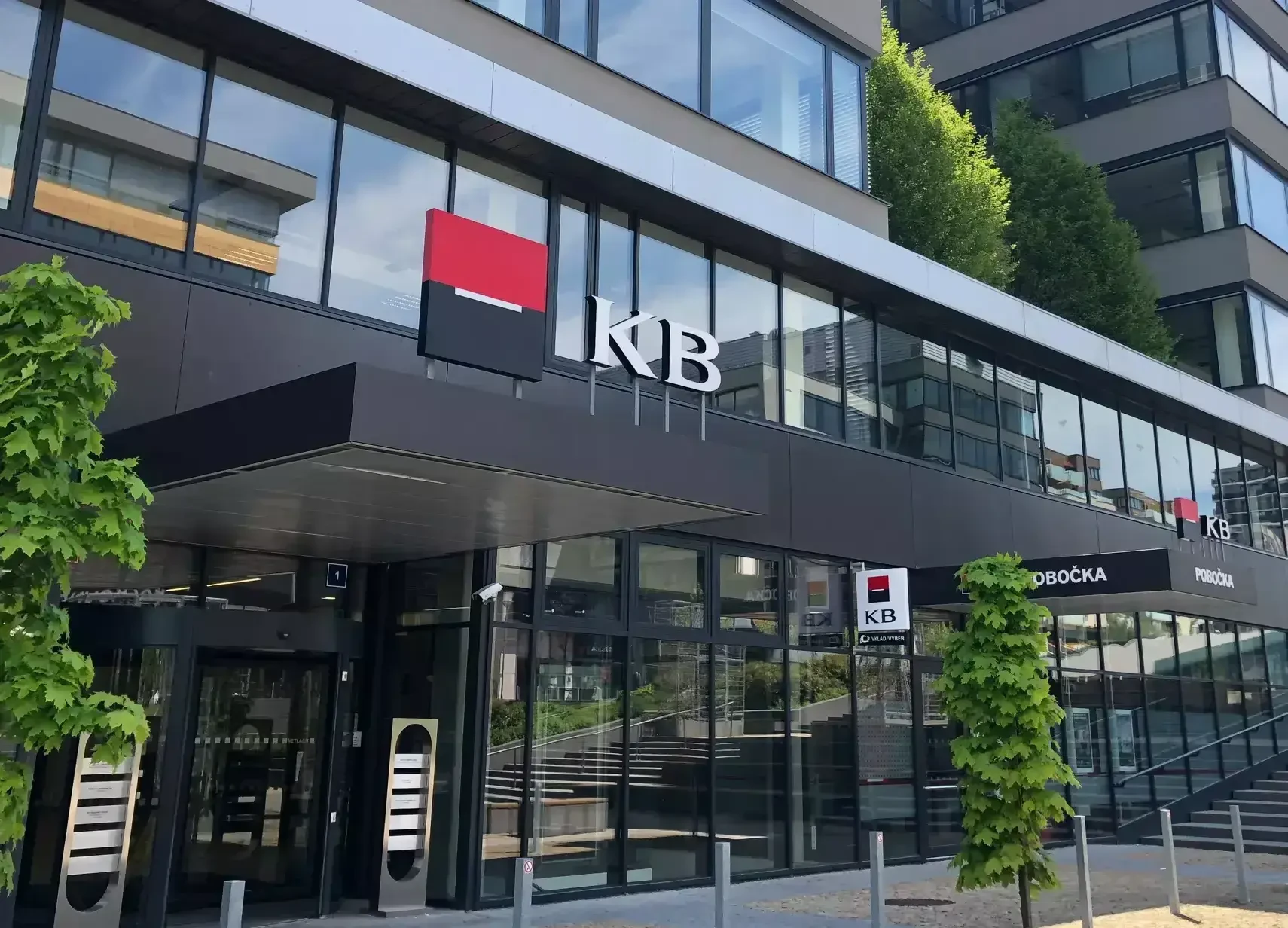 Illustrative photo of a modern Komerční banka branch with prominent KB logo – visual of an urban banking environment with clean architecture and deposit/withdrawal signage