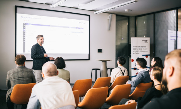 Přednáška o využití umělé inteligence v náboru, kde řečník prezentuje AI řešení před publikem odborníků v konferenční místnosti.