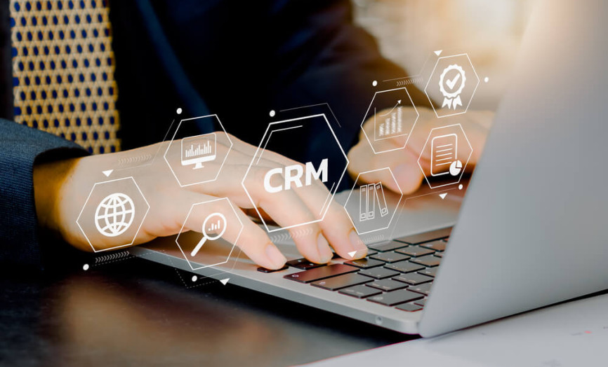 Osoba v business oblečení píše na notebooku, kolem ní jsou digitální ikony CRM a datových nástrojů v hexagonové mřížce