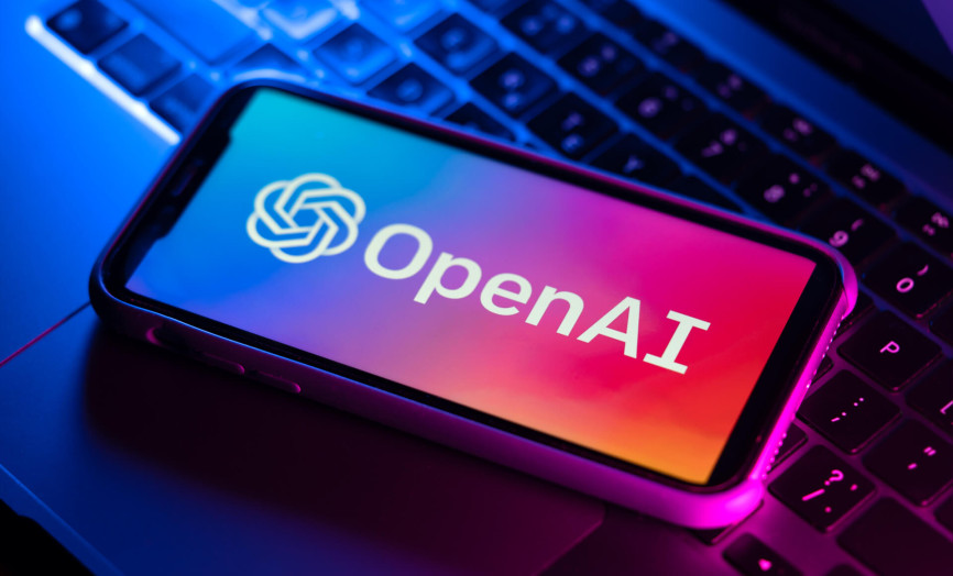Smartphone s logom OpenAI položený na klávesnici notebooku v neónovom osvetlení – symbol integrácie umelej inteligencie do mobilných zariadení a moderného digitálneho pracoviska.